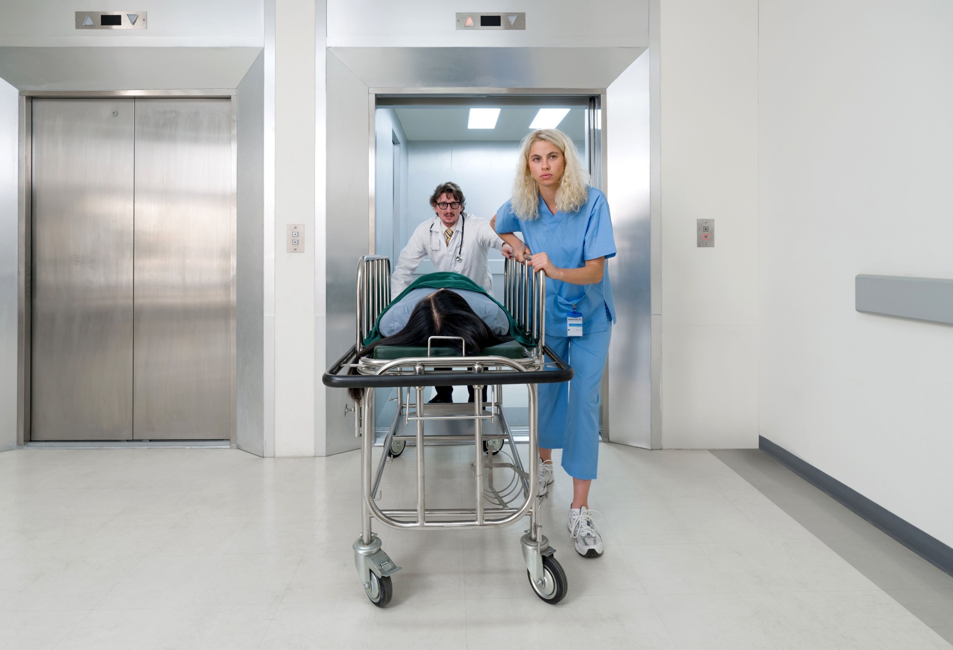 A nurse and doctor in propels a wheeled stretcher, carrying a patient out of the elevator to the emergency room of the hospital.